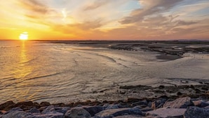 Ein Küsten-Sonnenuntergang mit felsiger Küste und ruhigem Wasser, das den Himmel spiegelt.
