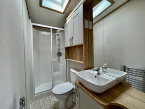 A compact bathroom with a glass-enclosed shower, a toilet, and a sink with a wooden countertop. - Prime Location 3-bed Chalet in Seal Bay, Selsey (Chichester)