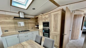 Eine moderne Küche mit Holzschränken, einem Gasherd und eingebauten Backöfen. Es gibt einen Esstisch mit Stühlen und ein Oberlicht.