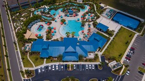 Oversigtsbillede af et resort med flere swimmingpools, en parkeringsplads og en stor bygning med et blåt tag.