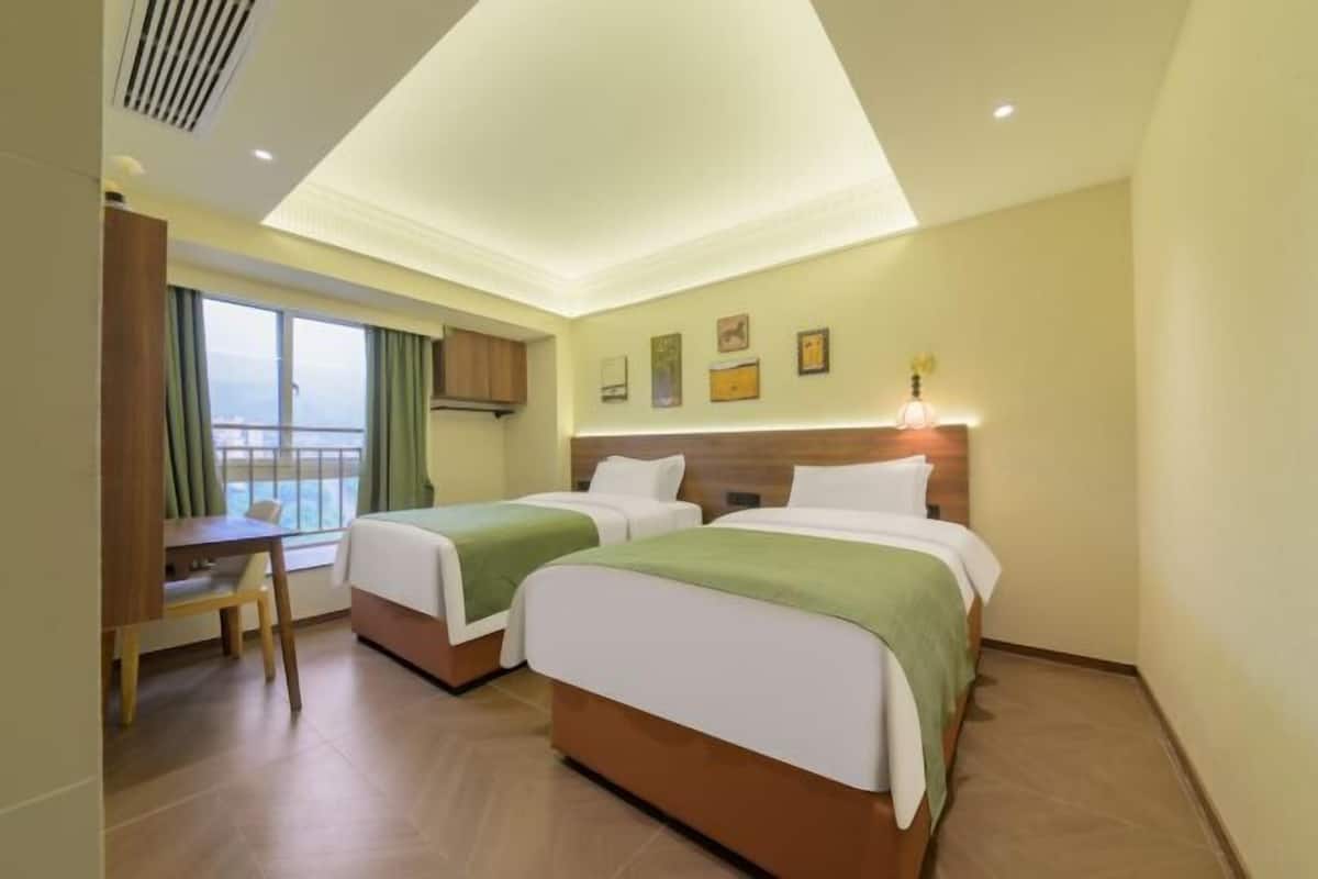 Une chambre d’hôtel avec deux lits, un bureau, une chaise et une fenêtre avec des rideaux.