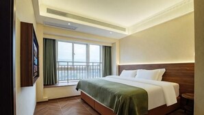 Een hotelkamer met een bed, een raam met gordijnen, uitzicht op zee en een houten vloer.