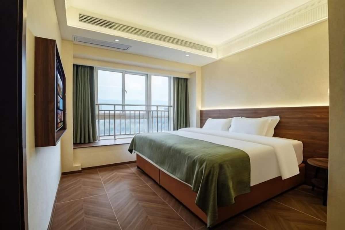 Une chambre d’hôtel avec un lit, une fenêtre avec des rideaux, une vue sur la mer et un plancher en bois.