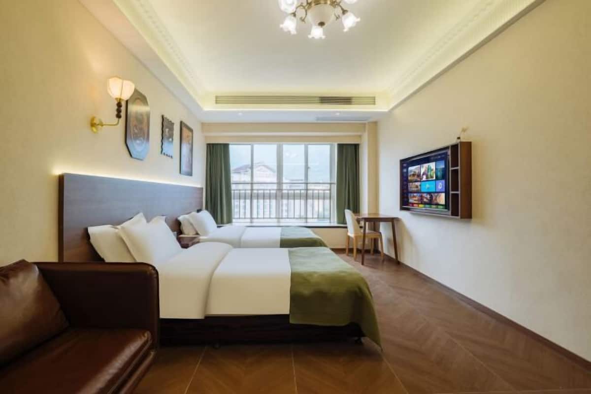 Une chambre d’hôtel avec un lit, un canapé, une télévision et une fenêtre avec des rideaux.