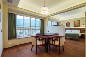 Une chambre d’hôtel avec une table à manger, des chaises, un lit recouvert d’une courtepointe verte, un balcon avec vue et un lustre.