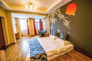 Quarto de hotel com uma cama grande, área de estar com uma poltrona e uma mesa, e parede com design decorativo.