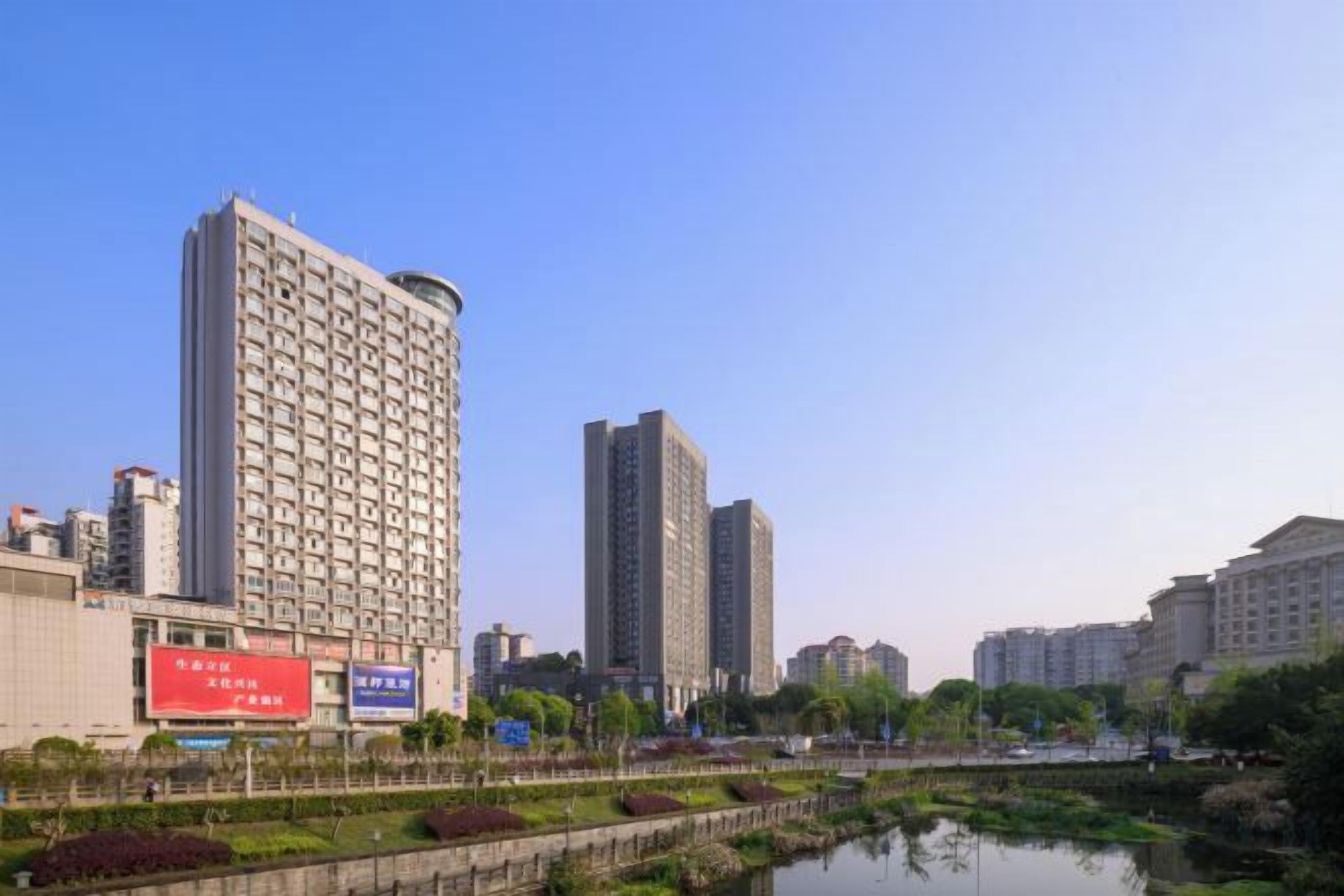 Um edifício alto com design moderno, rodeado por um corpo d'água tranquilo e vegetação.