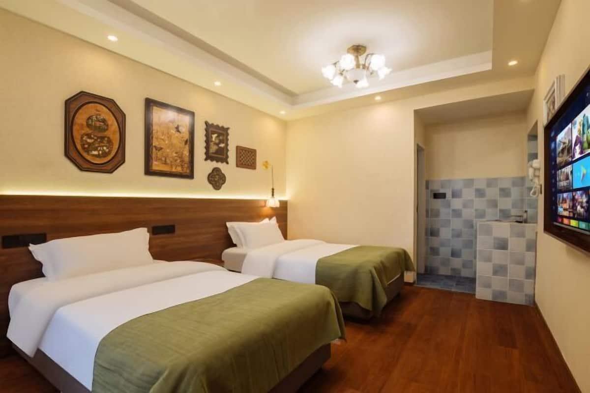 Une chambre d’hôtel avec deux lits, une tête de lit en bois, des œuvres d’art accrochées au mur, un luminaire au plafond et un mur recouvert de carreaux à motifs.
