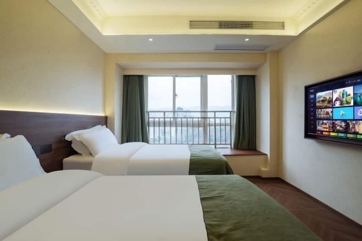 Une chambre d’hôtel avec deux lits, une grande fenêtre donnant sur un beau paysage et un téléviseur à écran plat fixé au mur.