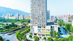 Een modern hoog hotel met meerdere verdiepingen, omgeven door groen en een helder uitzicht op de stad.