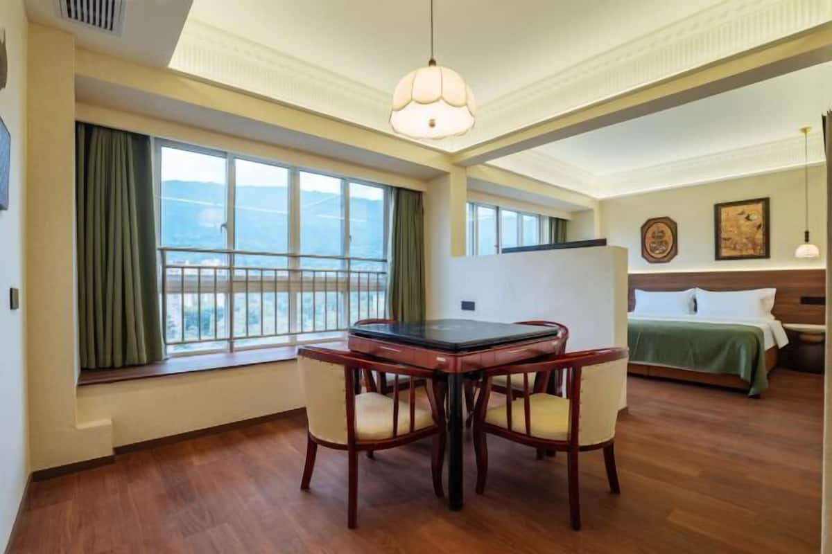 Une chambre d’hôtel avec un balcon, une table à manger avec des chaises, un lit et une grande fenêtre avec des rideaux.
