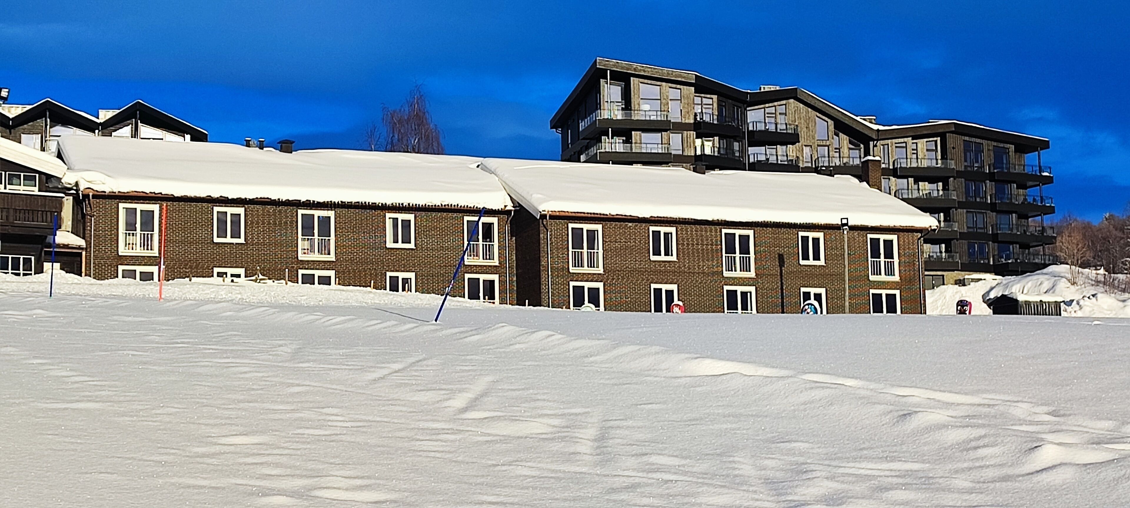 A snow-covered ski resort with modern multi-story buildings, ski lifts, and a clear blue sky.