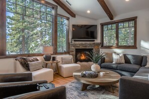 A cozy living room with a fireplace, large windows, and a comfortable seating area. - Exclusive Luxury Home, Two Private Hot Tubs & Peaceful Forest Setting (Mammoth Lakes)