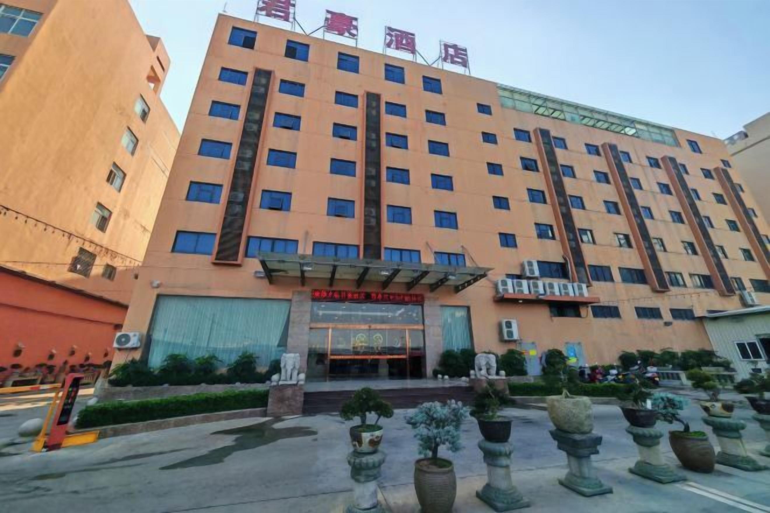 Un hotel de varios pisos con una entrada destacada, ventanas amplias y una zona cubierta con plantas en macetas.