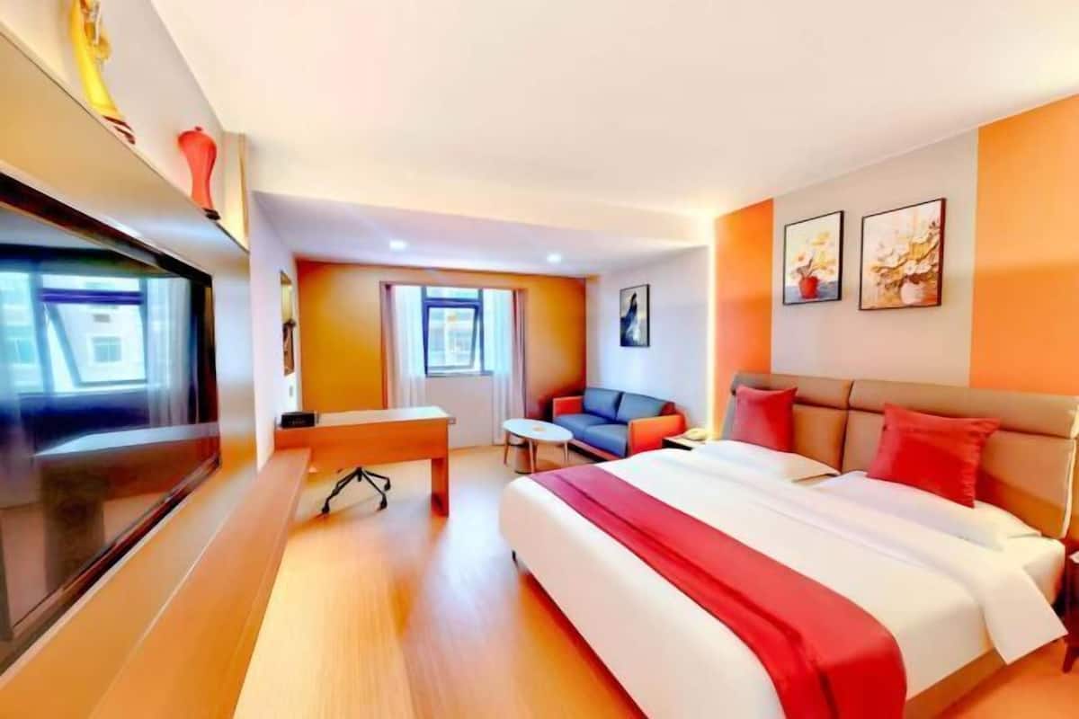 Ett hotellrum med en säng, ett skrivbord, en tv, en soffa och konstverk på väggarna.