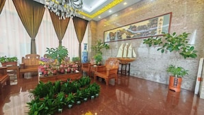 A lobby with a marble floor, wooden furniture, potted plants, and a painting on the wall. - Grandhall Hotel Shishi (Shishi)