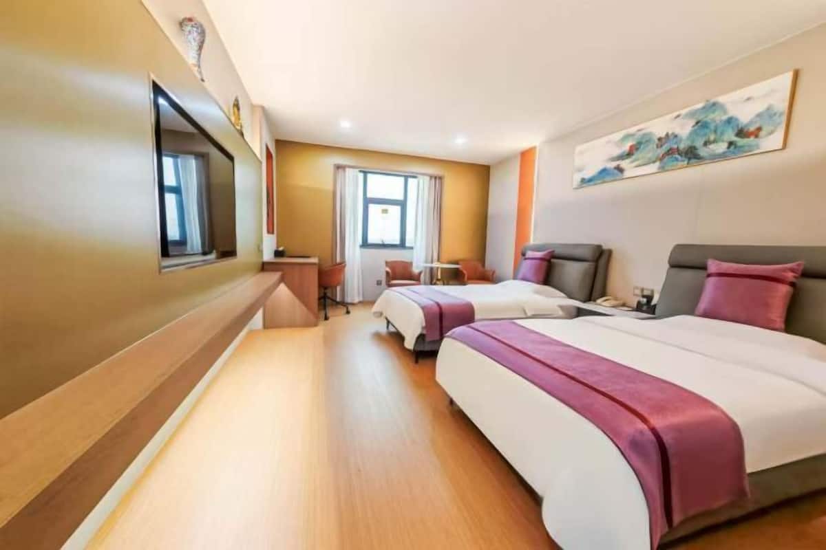 Ett hotellrum med två sängar, ett skrivbord, en stol, en tv och en tavla på väggen.