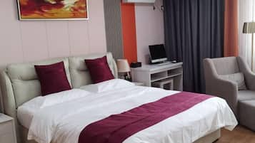 Ein Hotelzimmer mit einem Bett, einem Schreibtisch mit Computer, einem Stuhl und einem Fenster mit Vorhängen.