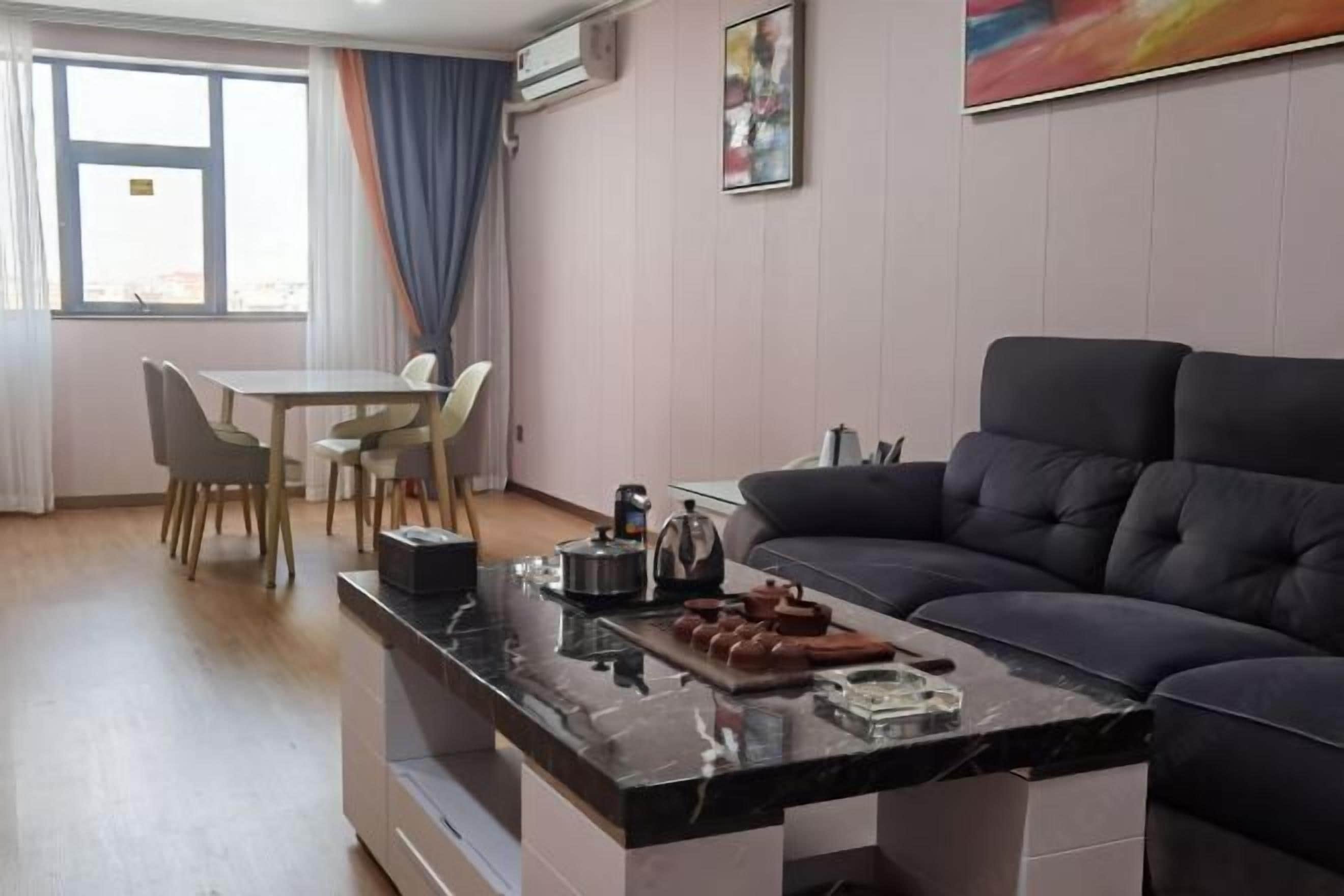 Ein modernes Wohnzimmer mit einem dunklen Sofa, einem Essbereich mit Tisch und Stühlen sowie einer Küchenzeile mit Kaffeemaschine und Snacks.