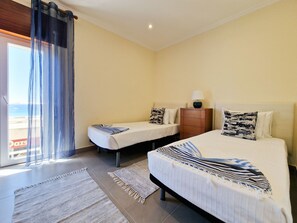 Habitación de hotel con dos camas, una mesita de noche de madera, una lámpara y vista al mar.
