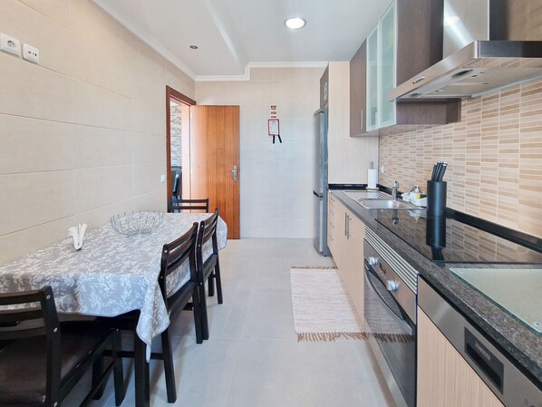 Una cocina moderna con comedor, que incluye una mesa de madera, sillas, un refrigerador y una campana extractora de acero inoxidable.