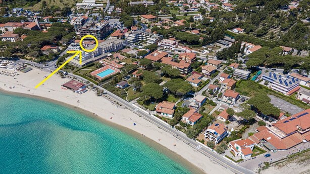 An aerial view of a coastal town with a beach, residential buildings, and a marked location with a yellow arrow. - Casa Bartolomea - CASA BARTOLOMEA 9 (Marina di Campo)