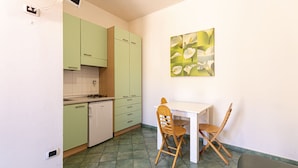 A compact kitchen with green cabinets, a white countertop, and a small dining area with two wooden chairs and a white table. - Casa Bartolomea - CASA BARTOLOMEA 9 (Marina di Campo)