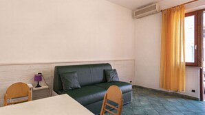 A room with a green sofa, a wooden table, a purple lamp, and a window with yellow curtains. - Casa Bartolomea - CASA BARTOLOMEA 9 (Marina di Campo)