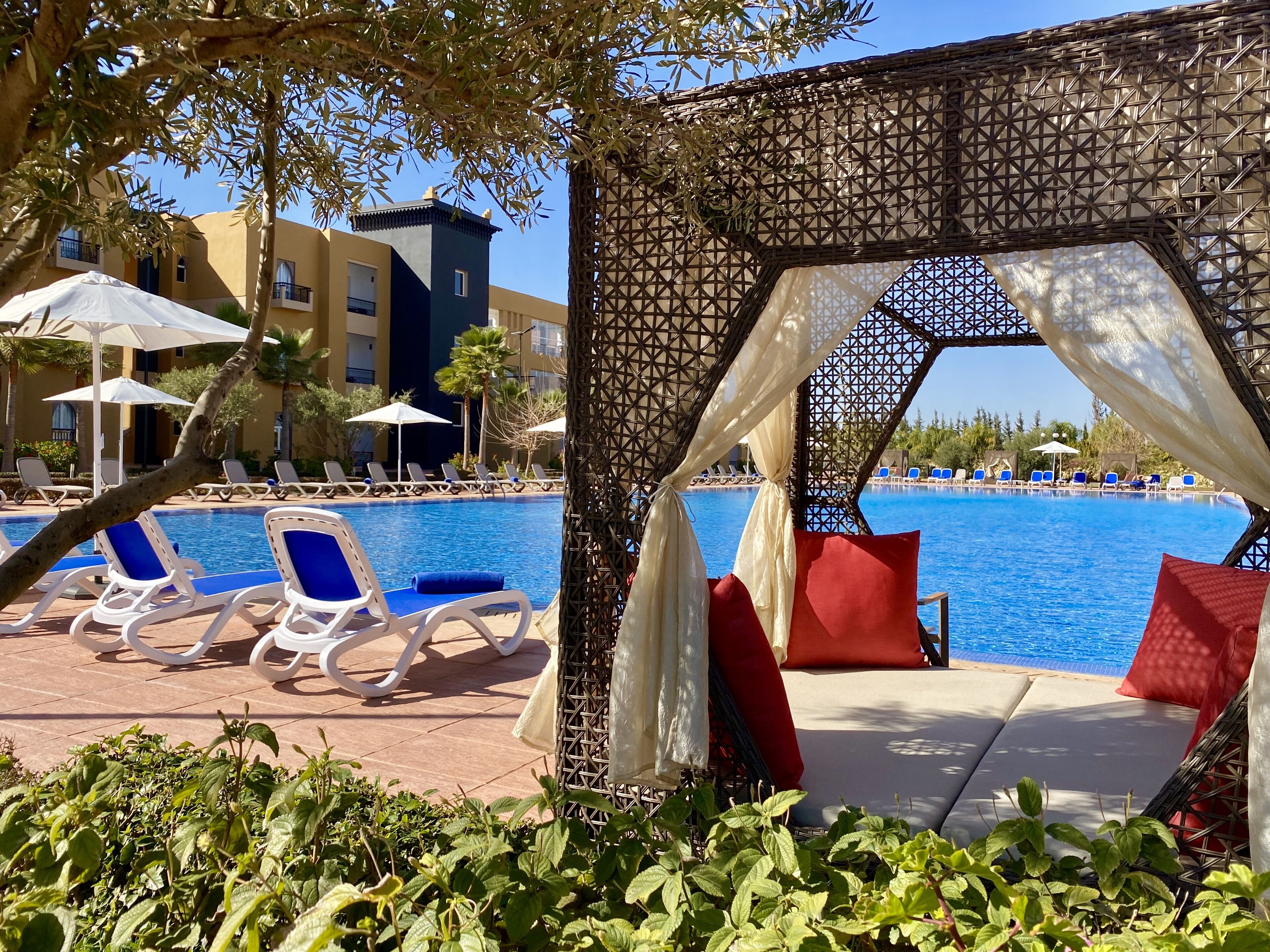 Un área junto a la piscina con sillas de descanso y un espacio de estar techado.