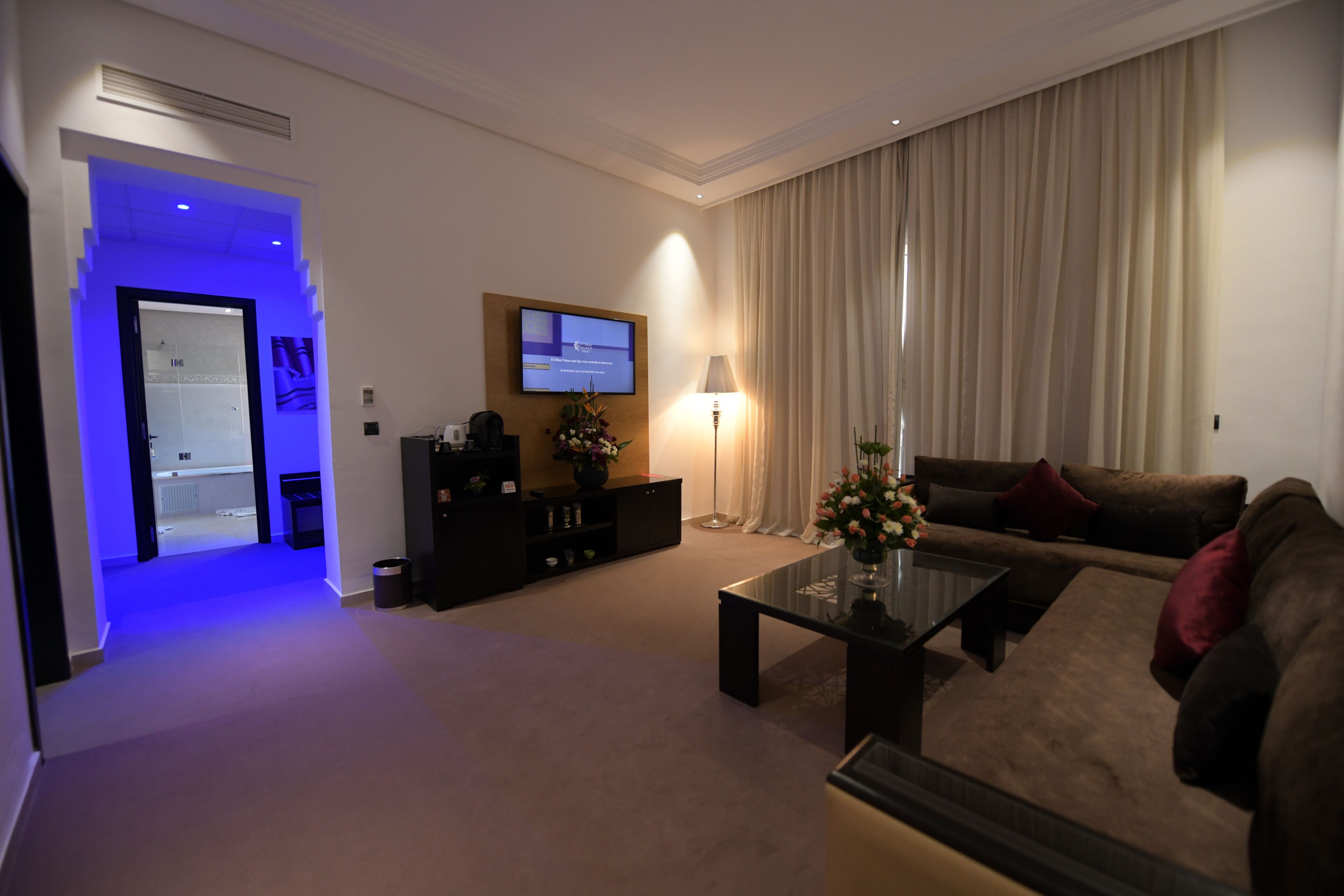 A modern living room with a sofa, coffee table, and TV. There is a lamp and a plant on the coffee table.