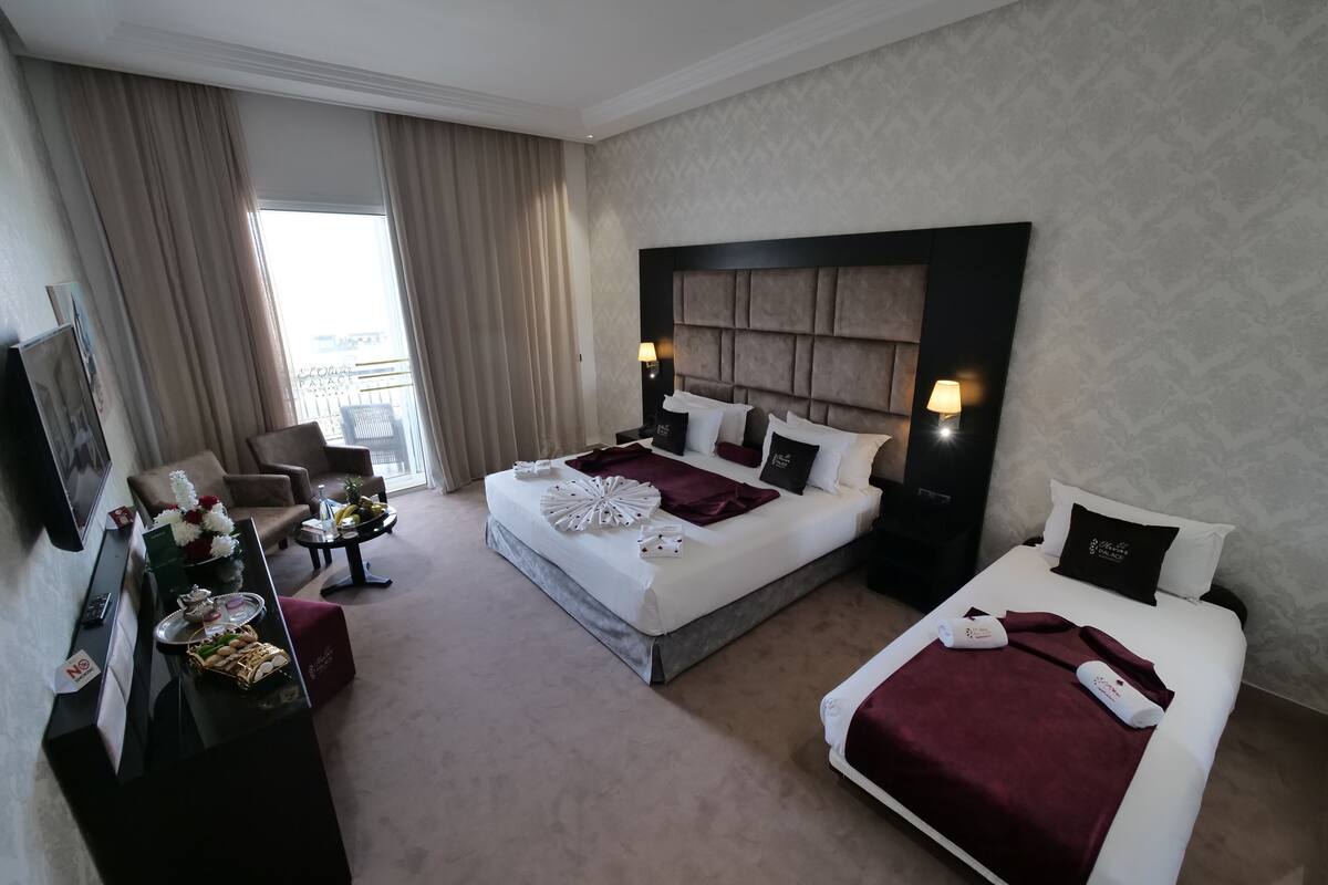 A hotel room with a large bed, a smaller bed, a desk with a lamp, a TV, and a view of the outside.