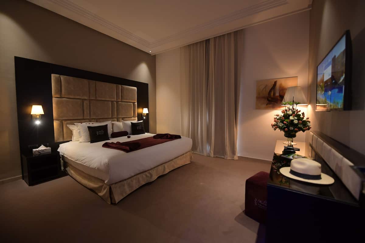 A hotel room with a large bed, a nightstand, a lamp, a painting, and a television.