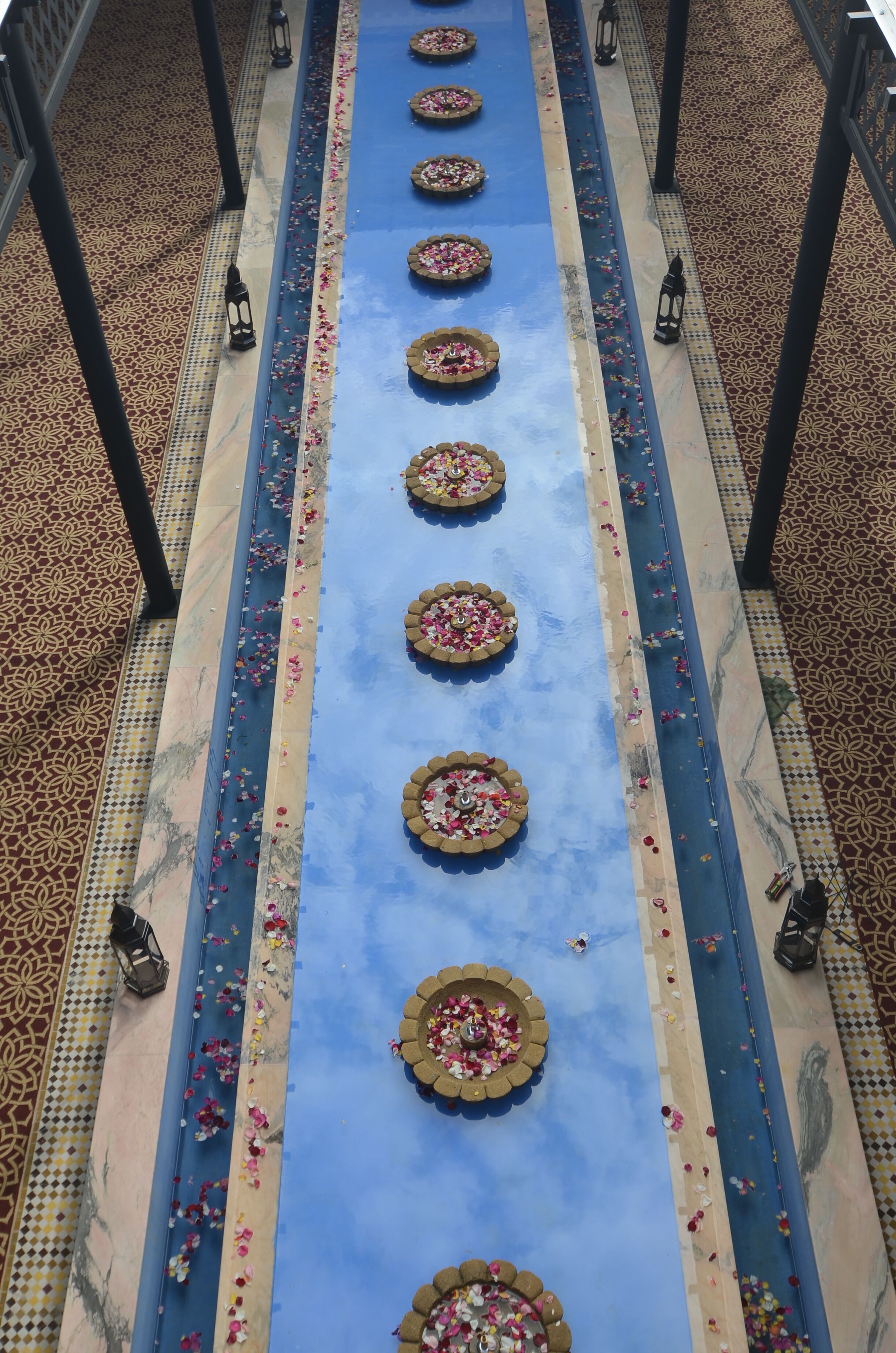 Un pasillo con alfombra azul, arreglos florales decorativos y baldosas con estampado.