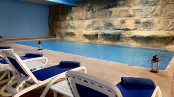 Une piscine intérieure aux murs en pierre, dotée de chaises longues bleues et décorée de lanternes.