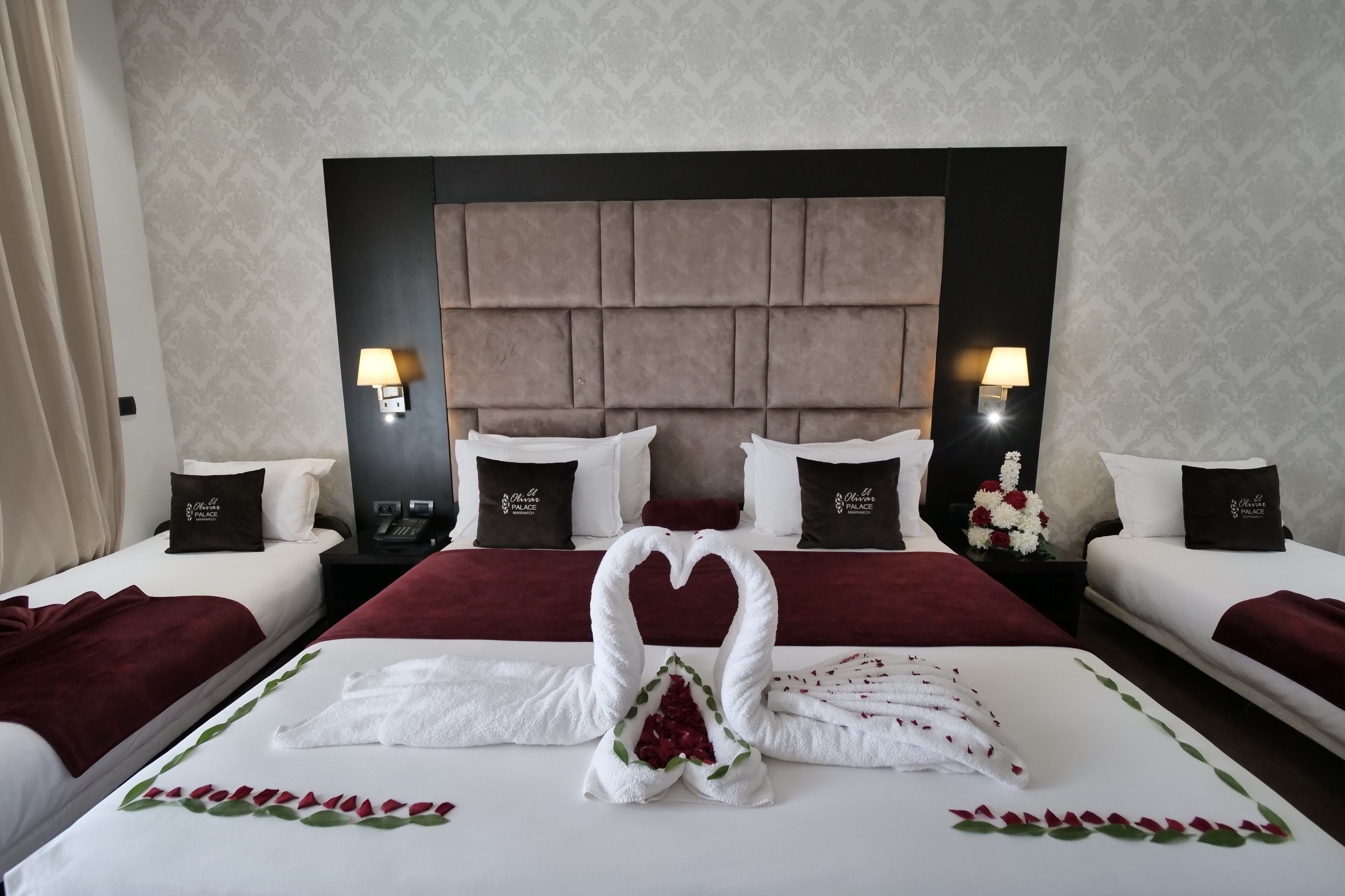 Habitación de hotel con dos camas, un cabecero grande y toallas decorativas con forma de cisnes.
