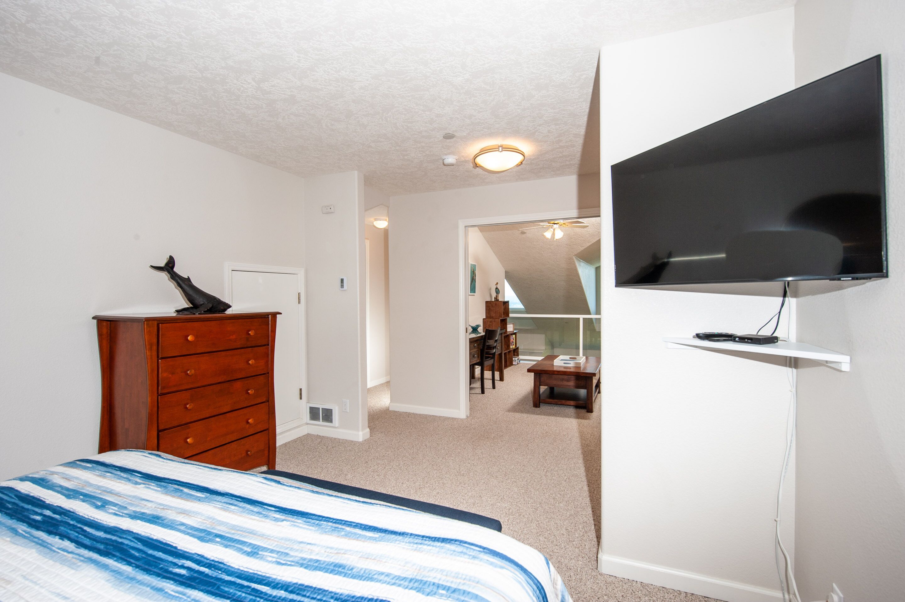 Une chambre à coucher avec un lit, une commode, une télévision et une vue sur une autre pièce.