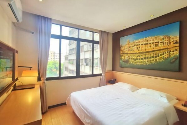 Habitación de hotel con cama, ventana con cortinas, un cuadro en la pared y escritorio con lámpara.