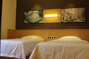 Dos camas individuales con ropa de cama blanca, una lámpara fijada a la pared y dos cuadros colgados encima de las camas.