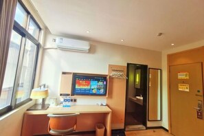 Habitación de hotel con escritorio, silla, aire acondicionado, televisión y puerta con espejo.