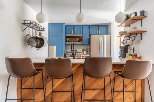 Une cuisine moderne avec des meubles bleus, un îlot central doté de tabourets de bar, des ustensiles de cuisine suspendus et un plancher en bois.