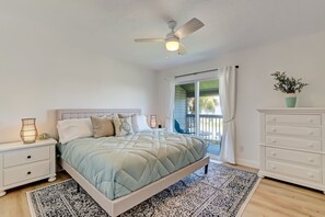 Ein Schlafzimmer mit Bett, Nachttisch, Kommode, Deckenventilator und Blick ins Freie.