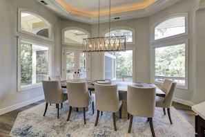A dining area with a round table, six chairs, and a chandelier.