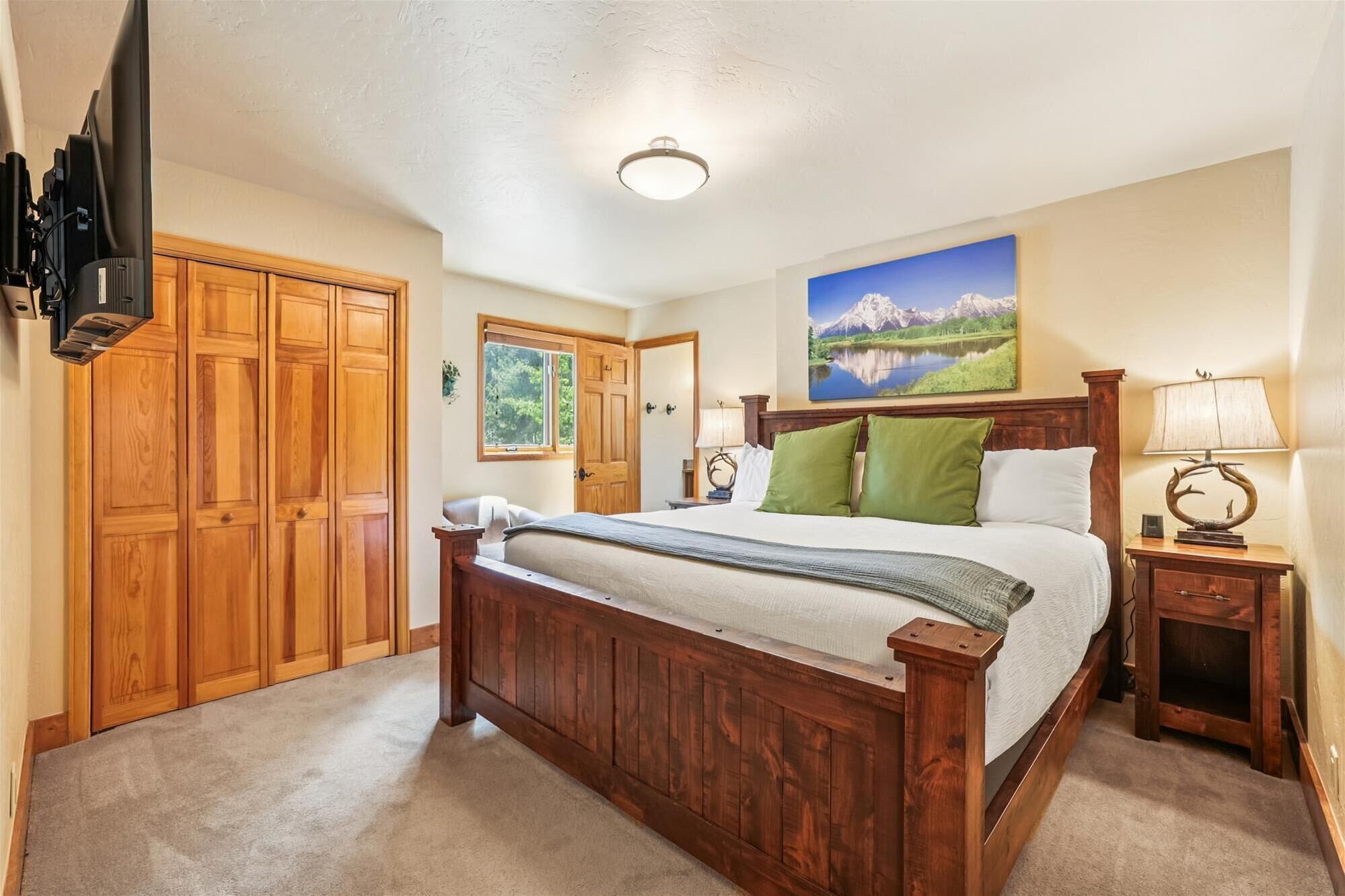Un dormitorio con cama de madera, un cuadro de un lago y un televisor montado en la pared.