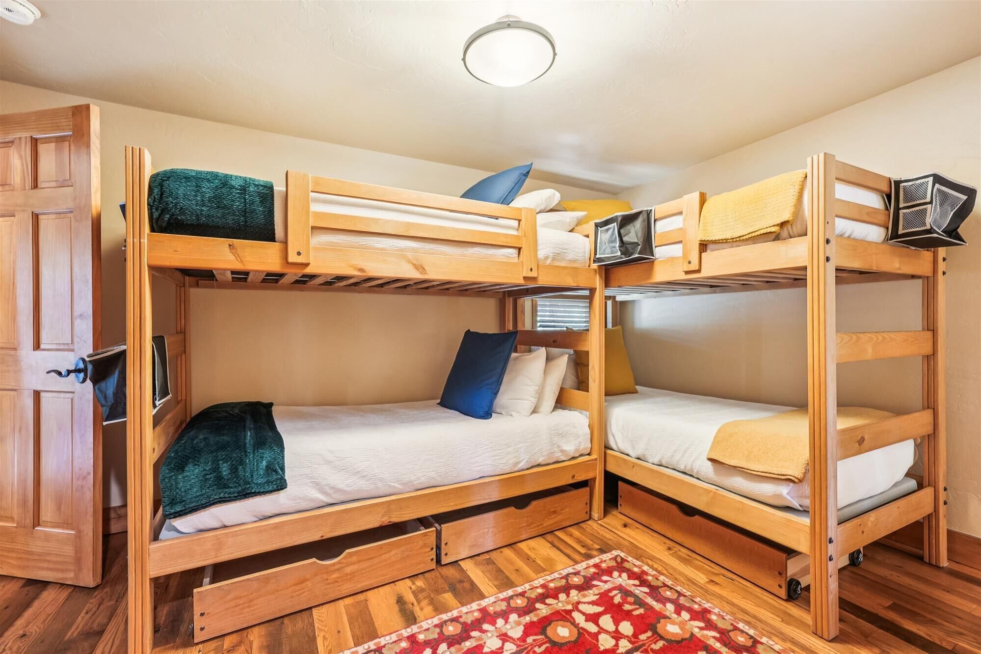 Een slaapkamer met stapelbedden, een houten vloer, een rood tapijt met een patroon en een deur met een handvat.