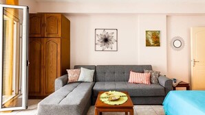 Una sala de estar con un sofá gris, un aparador de madera, una mesita con un mantel individual y una cama azul.