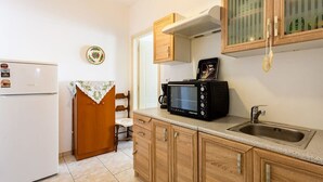 Una cocina compacta con refrigerador blanco, microondas, pileta, muebles de madera y un pequeño comedor con una silla y una mesa.