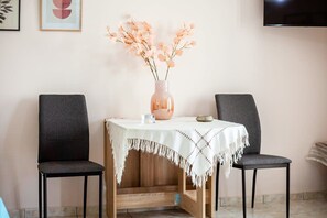 A dining area with a table set for two, a vase with flowers, and a television mounted on the wall.