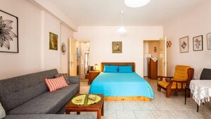Una habitación acogedora con cama, sofá, mesa de comedor y una silla. Hay un cuadro en la pared y una lámpara sobre la mesa.