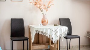 Un comedor con una mesa dispuesta para dos, un jarrón con flores y un televisor montado en la pared.