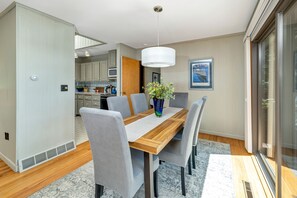 A dining area with a wooden table, grey upholstered chairs, a vase with flowers, and a modern pendant light.